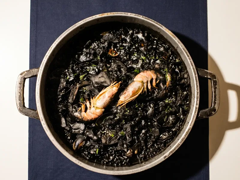 Arroz negro en la paellera, con dos cigalas encima y perejil picado sobre el arroz teñido de tinta.