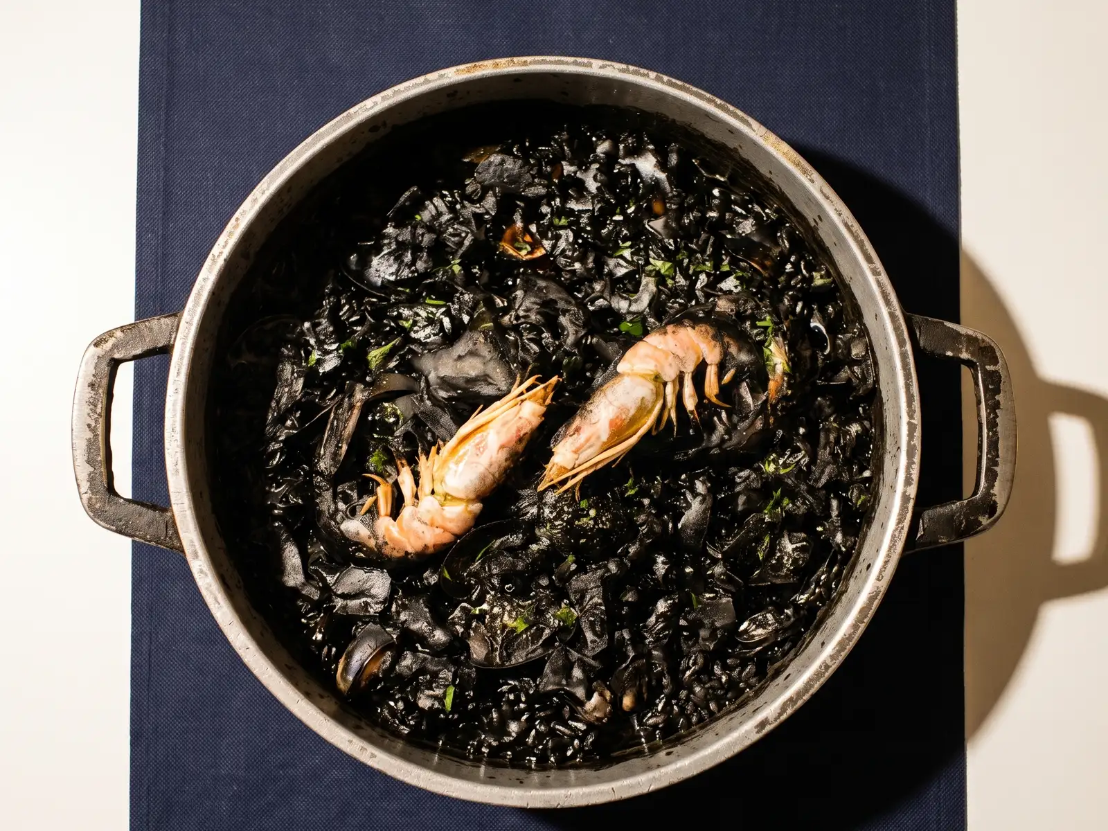 Arroz negro en la paellera, con dos cigalas encima y perejil picado sobre el arroz teñido de tinta.