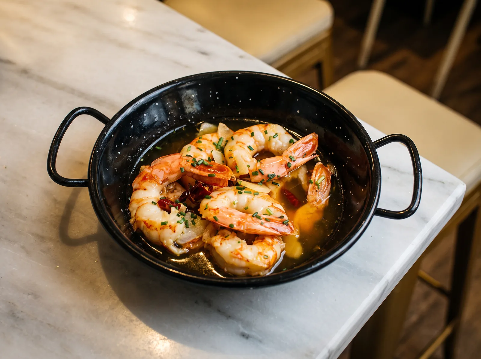 Gambas al ajillo en su cazuela negra, con láminas de ajo, guindilla y cebollino, sobre el mármol.