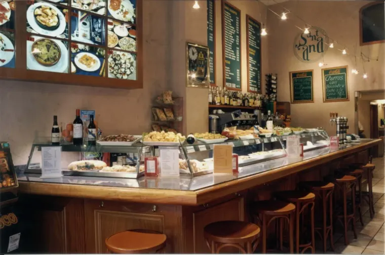 La barra de tapas antes de la reforma: las bandejas en la vitrina, los taburetes de madera y las pizarras de precios en pesetas al fondo.