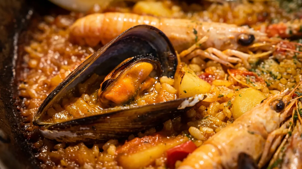 Primer plano de una paella de marisco, con un mejillón abierto, una cigala y una gamba sobre el arroz con azafrán.