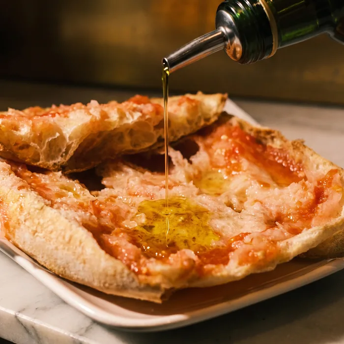 Un chorro de aceite de oliva cae sobre el pan con tomate, en un plato blanco.