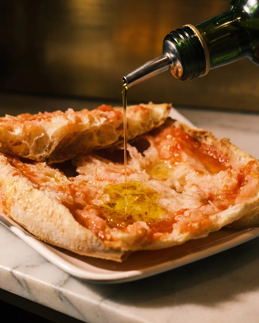 Un chorro de aceite de oliva cae sobre el pan con tomate, en un plato blanco.
